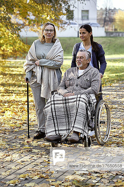 Ältere Frau spricht mit Krankenschwester und behindertem Mann  der im Rollstuhl im Park sitzt