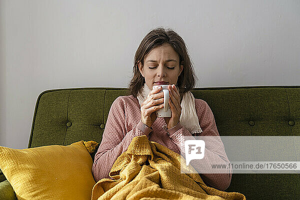 Kranke Frau mit Teetasse sitzt zu Hause auf dem Sofa