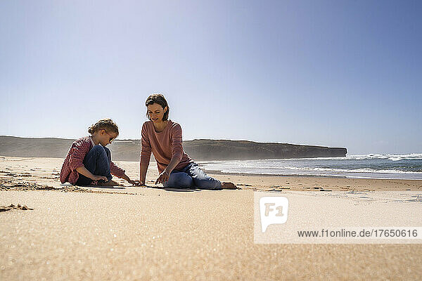 Happy mother and daughter playing with sand at beach on sunny day