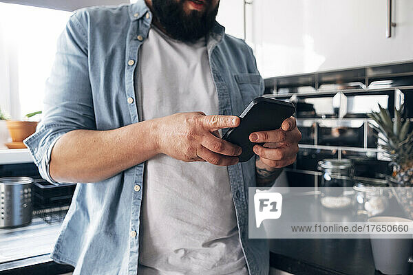 Mann benutzt Smartphone in der heimischen Küche