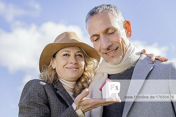 Smiling mature couple holding small house model on sunny day