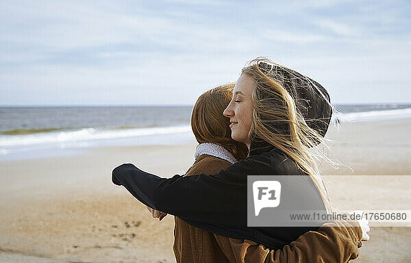 Young woman with eyes closed hugging sister on beach