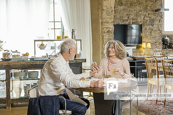 Smiling senior couple enjoying breakfast sitting at table in boutique hotel