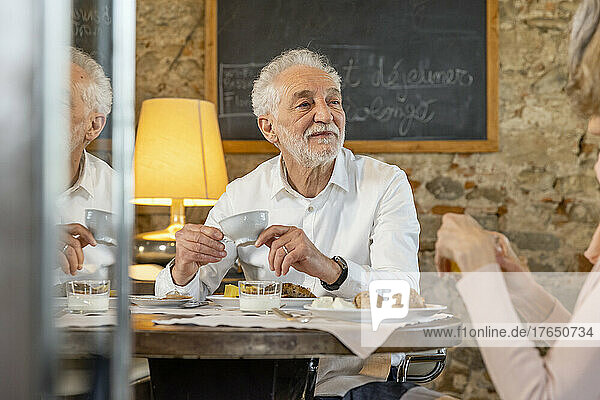 Älterer Mann mit Kaffeetasse sitzt mit Frau am Frühstückstisch im Boutique-Hotel