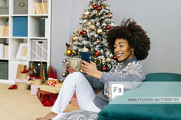 Happy woman with coffee cup sitting by sofa at home