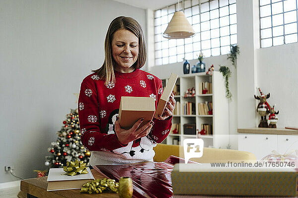 Smiling woman looking at gift box in living room
