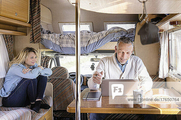 Man using laptop by woman sitting in motor home on weekend