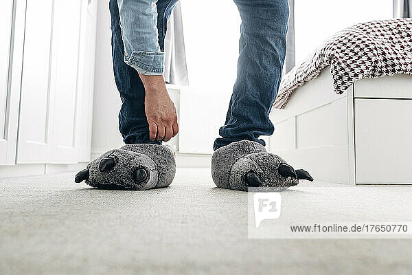 Man wearing wolf paw slippers in bedroom at home