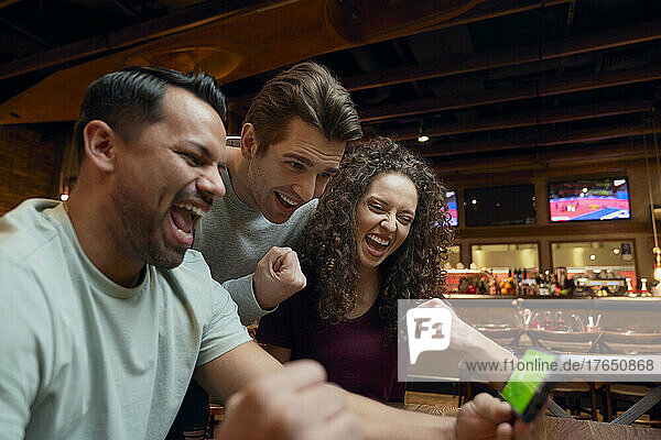 Cheerful soccer fans watching a match on smartphone in a pub
