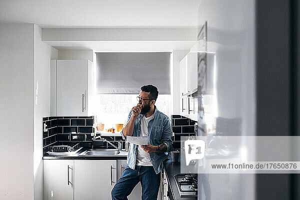 Freelancer with documents leaning on kitchen counter at home