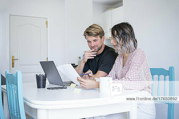 Freelancer discussing over document with woman sitting at dining table