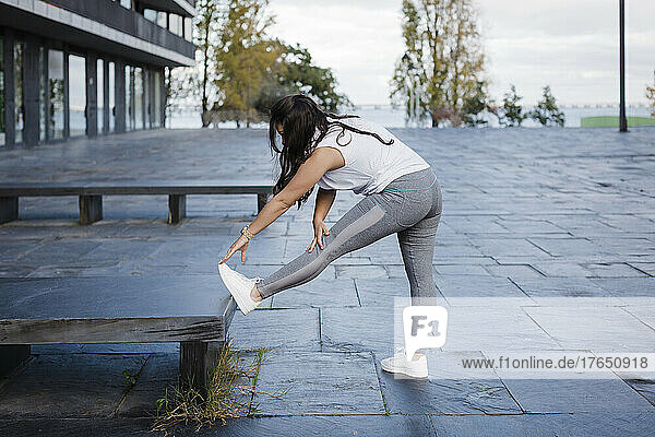 Woman doing stretching leg exercise by concrete seat