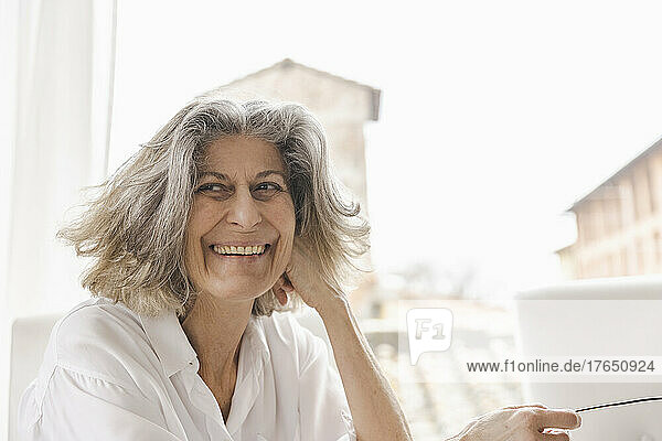 Happy senior woman sitting in front of window at home