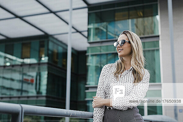 Contemplative businesswoman with sunglasses in front of office building