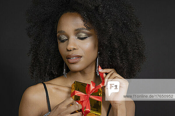 Beautiful young woman holding gift box against black background