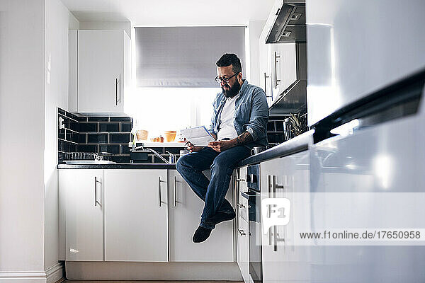 Freelancer with documents sitting on kitchen counter at home