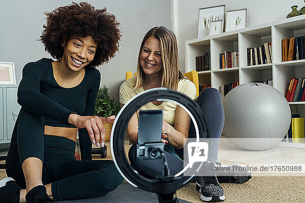 Happy young influencer with friend vlogging in living room at home