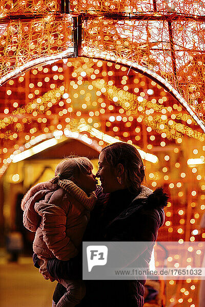 Mother embracing daughter standing by Christmas lights