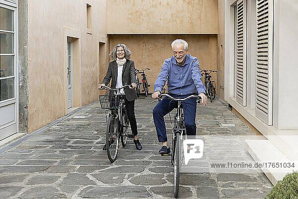 Smiling senior couple riding bicycles on footpath