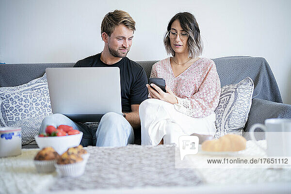 Frau diskutiert über Smartphone mit Mann  der zu Hause auf dem Sofa sitzt