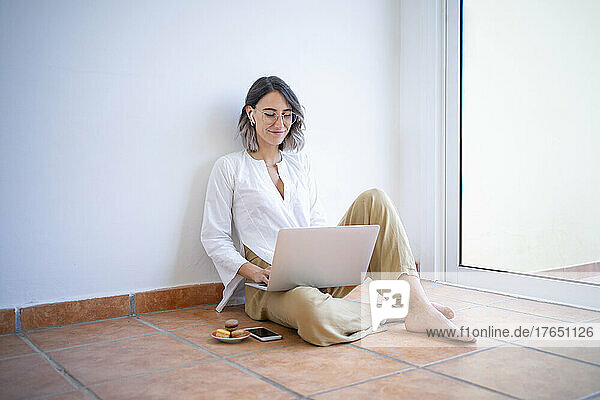 Smiling freelancer using laptop sitting by window at home