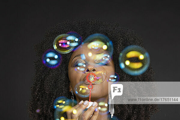 Young woman blowing soap bubbles against black background