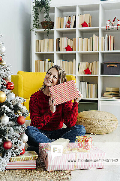 Glückliche Frau mit Weihnachtsgeschenken sitzt zu Hause