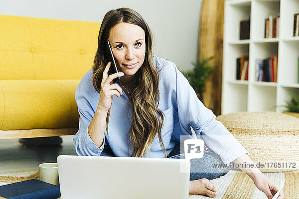 Freelancer with laptop talking on mobile phone at home