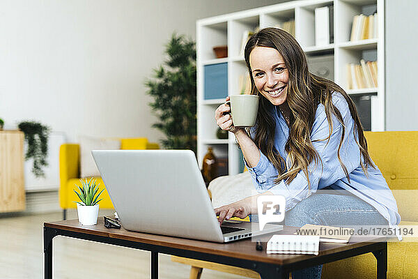 Happy Freelancer with coffee cup and laptop working at home