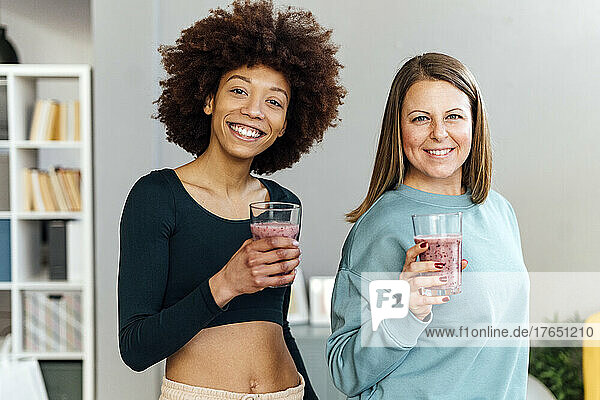Happy women holding glasses of smoothie standing in living room at home