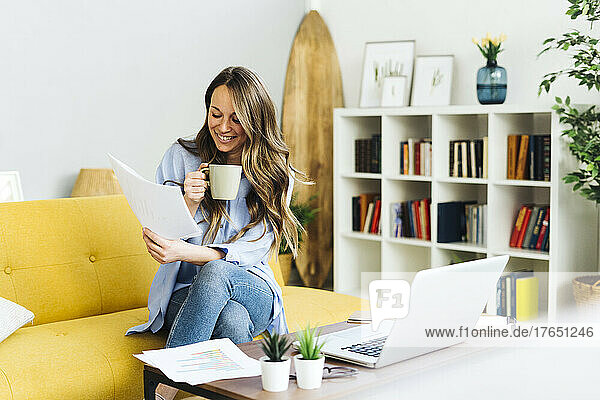 Smiling freelancer with coffee cup examining documents at home