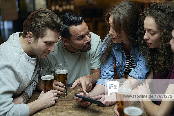 Group of friends having beer and sharing a smartphone in a pub