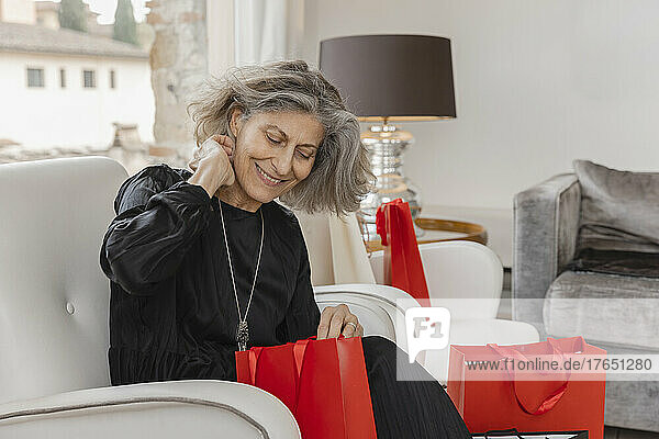 Happy senior woman with shopping bags sitting on armchair at boutique hotel