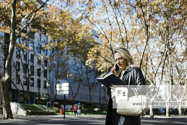 Woman talking on smart phone and reading diary in city