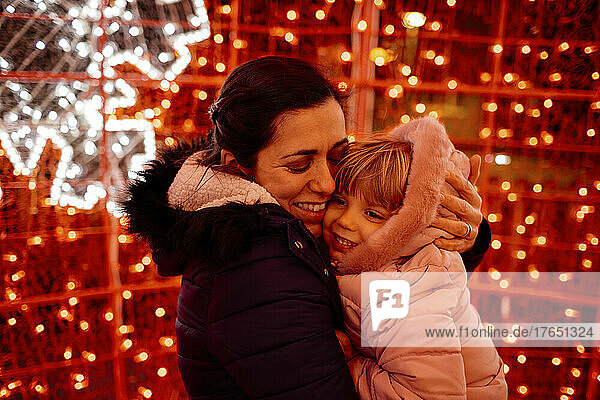 Happy mother hugging daughter in front of Christmas lights