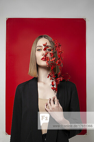 Blond woman holding twig in front of blank red frame against white background