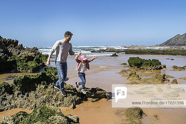 Happy father and daughter having fun on rocky beach