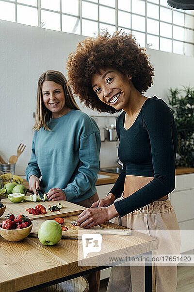 Happy young woman with friend cutting fruits in kitchen at home