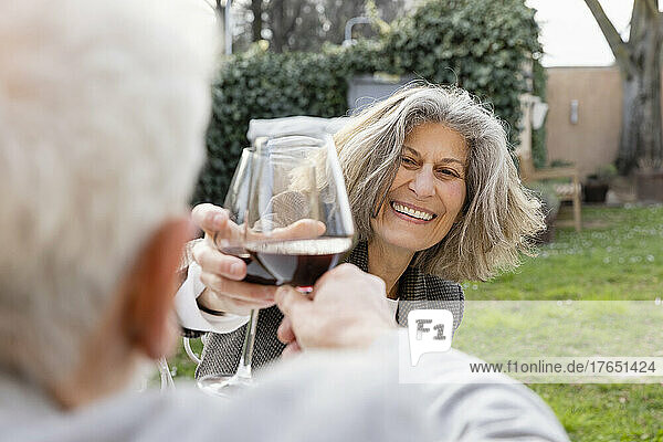 Glückliches älteres Paar  das im Garten sitzt und Weingläser anstößt