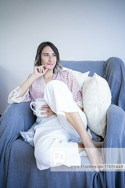 Smiling woman with macaroon and coffee mug sitting on sofa in living room