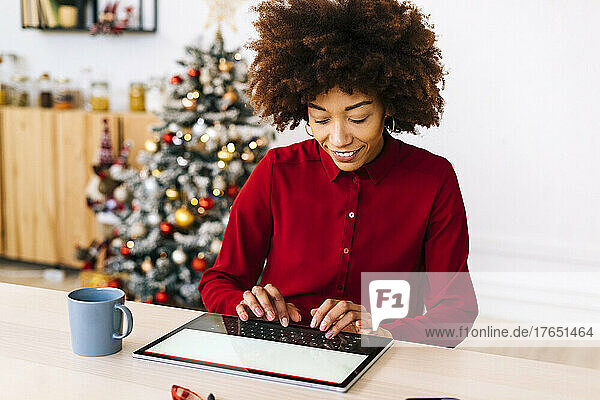 Glückliche Frau sitzt am Tisch im Wohnzimmer und benutzt einen Tablet-PC
