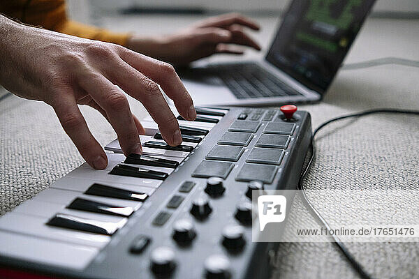 Hands of freelancer using laptop and piano in home studio