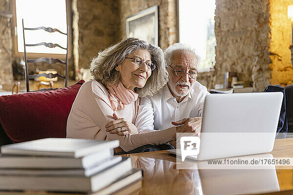 Lächelndes älteres Paar schaut auf den Laptop und sitzt auf dem Sofa im Boutique-Hotel