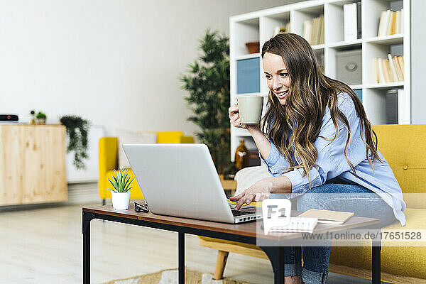 Smiling freelancer with coffee cup and laptop working at home