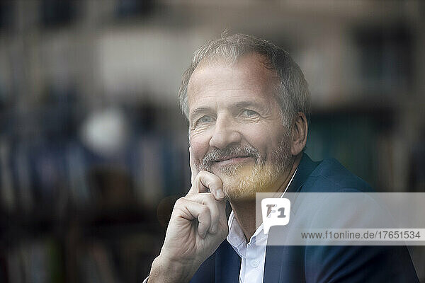 Smiling businessman with hand on chin looking through glass window