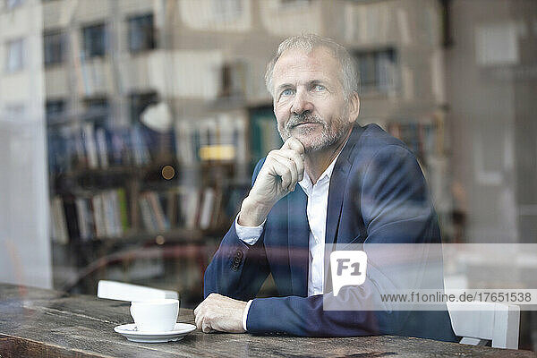 Businessman with hand on chin sitting at table by glass window