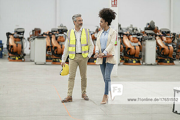 Engineer holding hardhat walking with businesswoman in factory