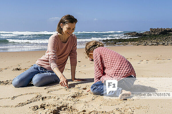 Glückliche Mutter und Tochter schreiben auf Sand am Strand