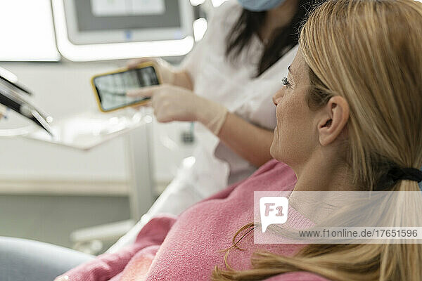 Dentist explaining x-ray image on mobile phone to patient at dental clinic