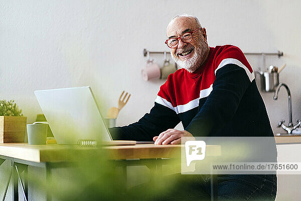 Happy senior man wearing eyeglasses sitting with laptop at home